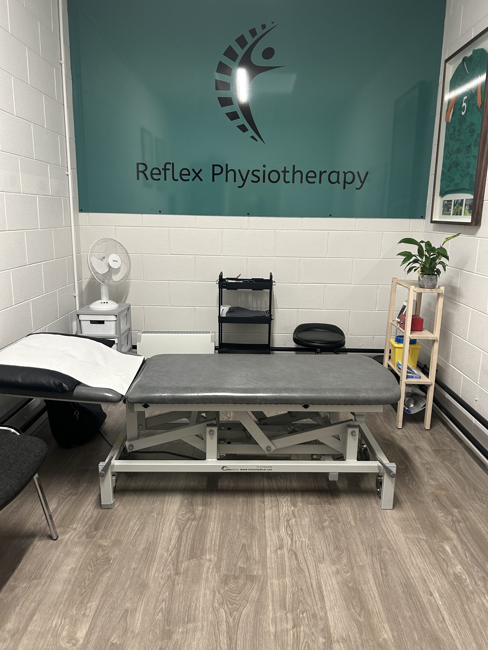 A Reflex Physiotherapy treatment room with a treatment couch under the Reflex logo