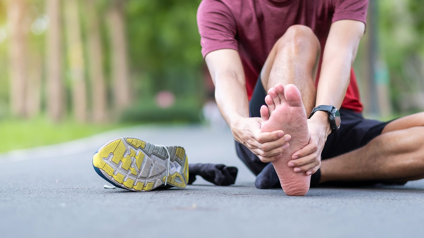 A person sitting on a path holding the sole of their foot