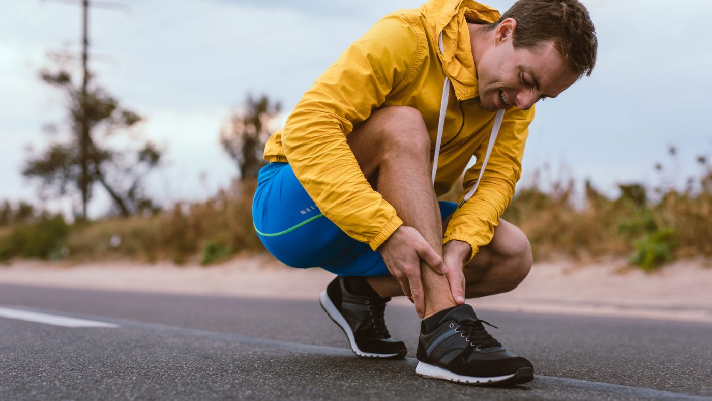 A runner crouching and holding his lower leg