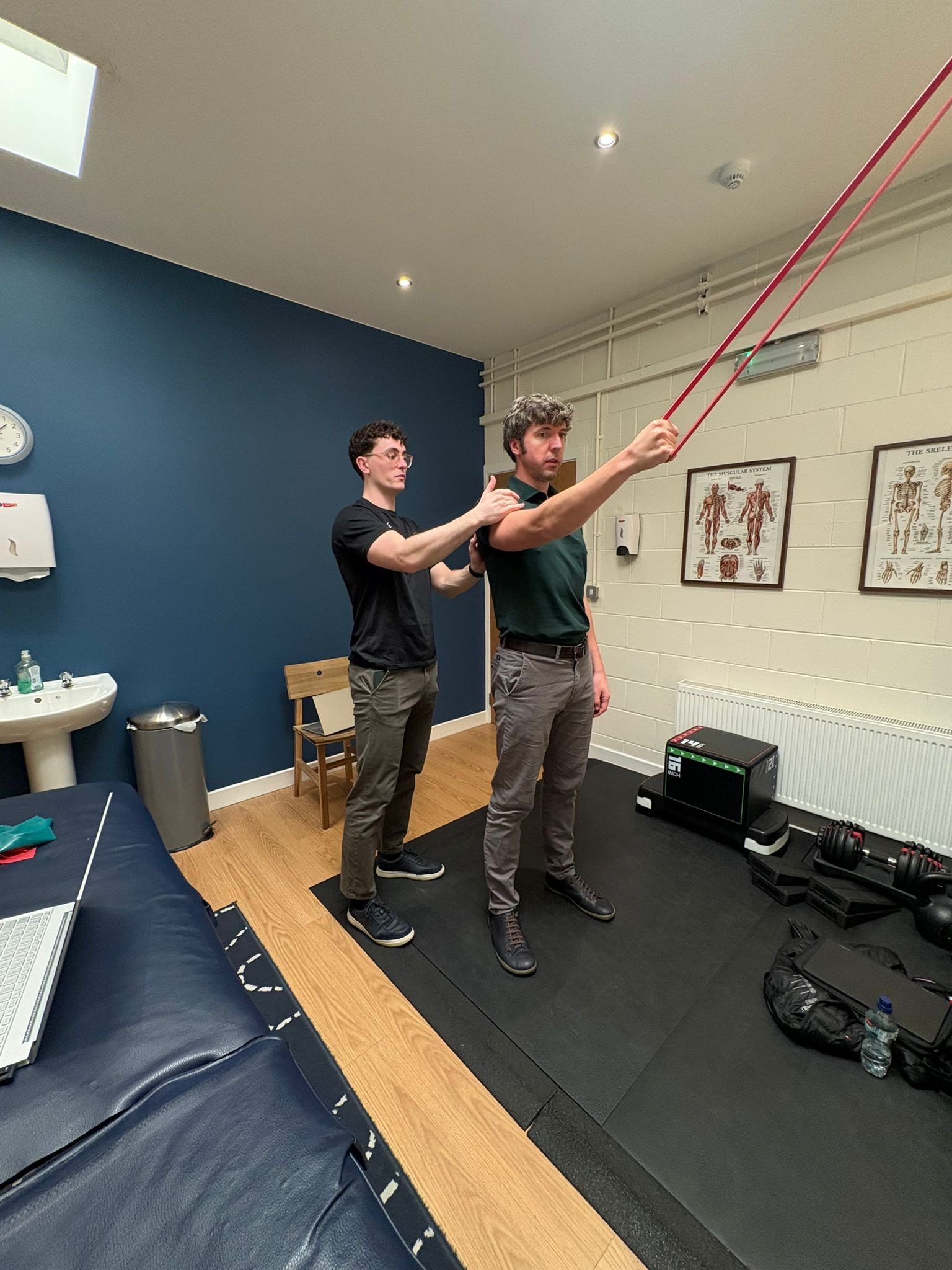 A Reflex therapist guiding a patient's shoulder through a resistance band exercise in the clinic